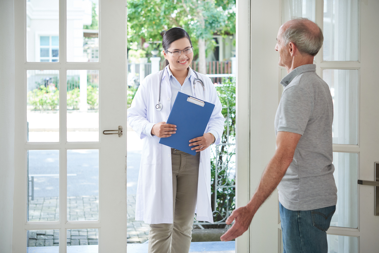 Elderly man opening door to smiling doctor making visit at home