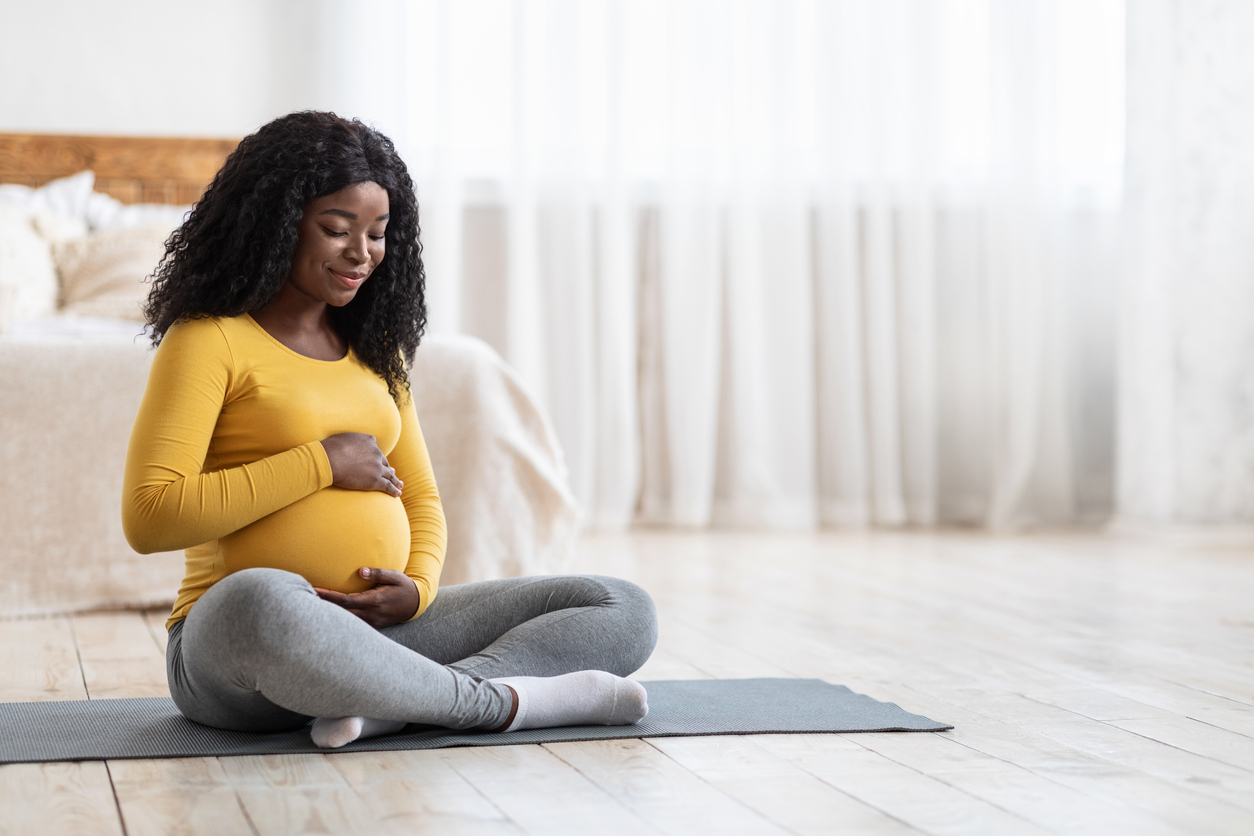 Pregnant african american woman doing morning yoga at home, touching her big tummy, copy space. Young expecting black lady having healthy lifestyle during pregnancy, exercising at bedroom