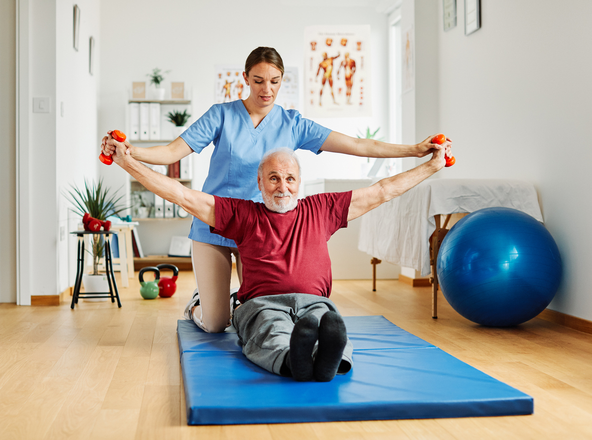 Doctor or nurse caregiver exercise with senior man at clinic or nursing home