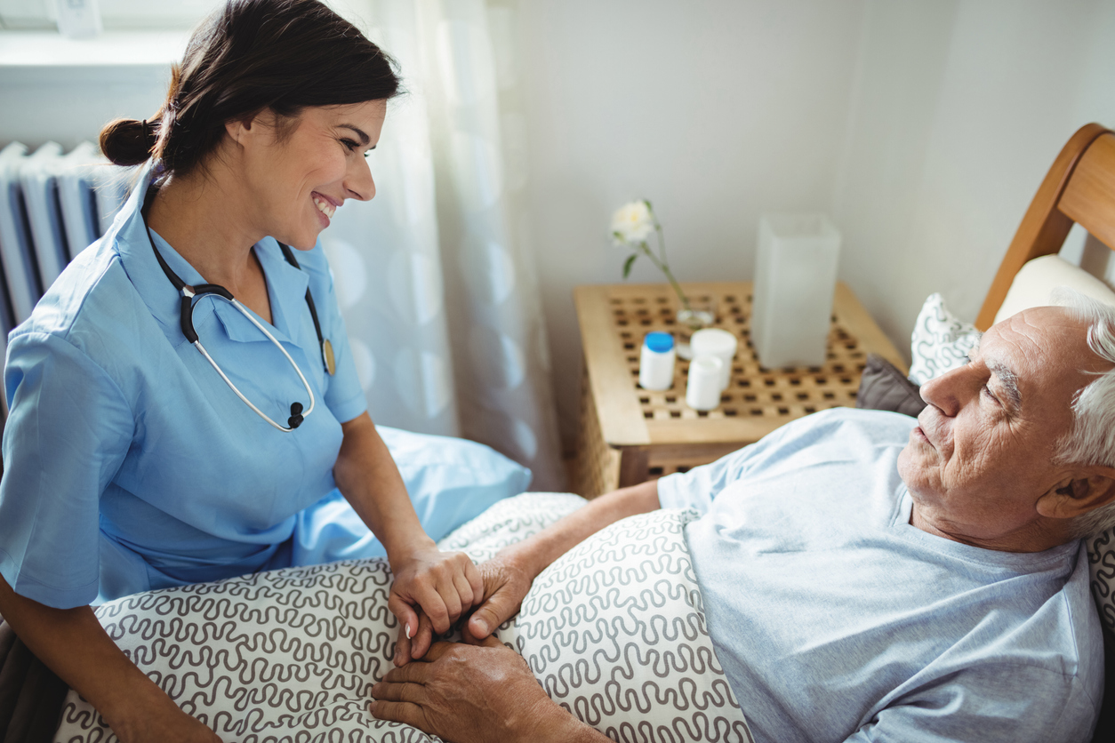 Nurse holding hands of senior man in bedroom